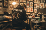 Tattoo artist working on a client in a tattoo parlor with tattoo designs on the wall.