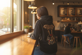 Person wearing a Traveler Tattoo hoodie with a tattoo design in a cafe